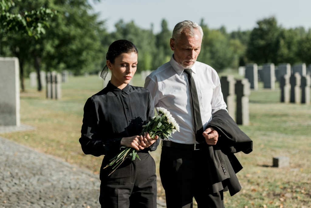 bearded senior man walking near woman with flowers on funeral